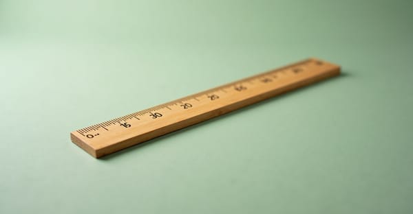 Wooden ruler lying diagonally on sage green background with shallow depth of field — measurement over optimization.